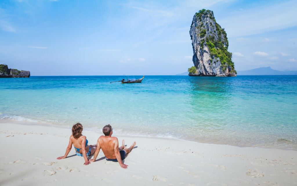 A happy couple sitting on a sandy beach, enjoying the scenic view of sea.