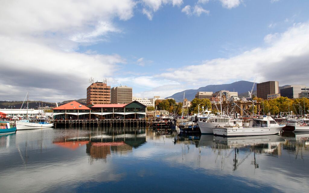 A scenic view of Hobart's waterfront, showcasing boats, buildings, and mountains in the background. Tasmania's picturesque port city.
