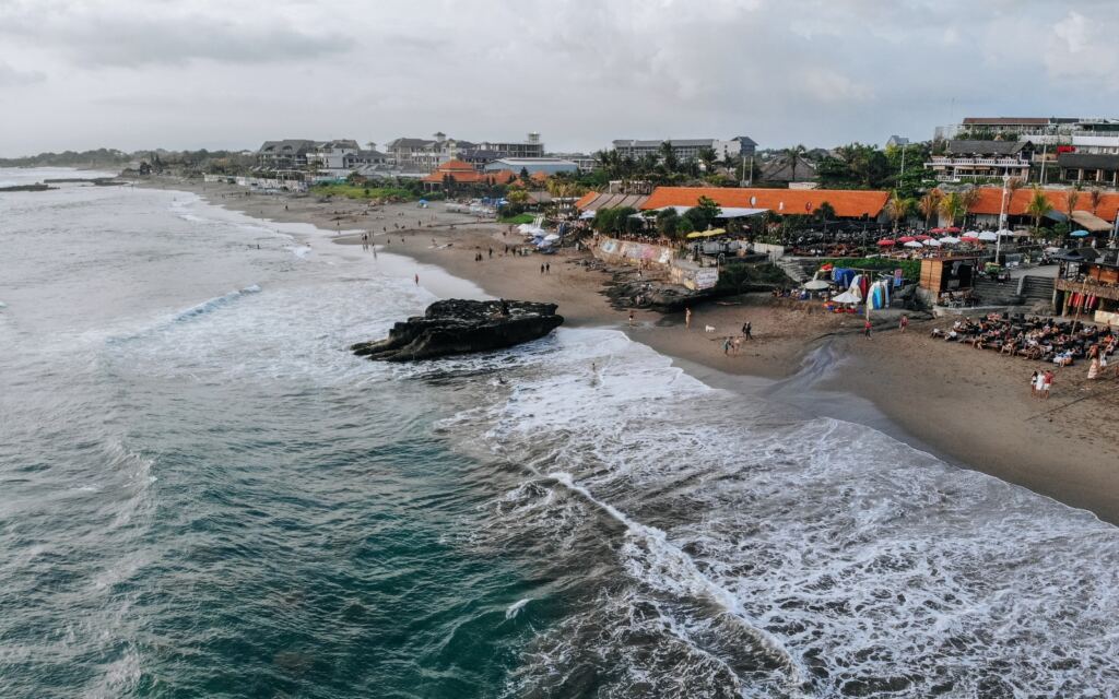 Aerial view of Canggu beach with surfers and umbrellas located in the west of Bali.