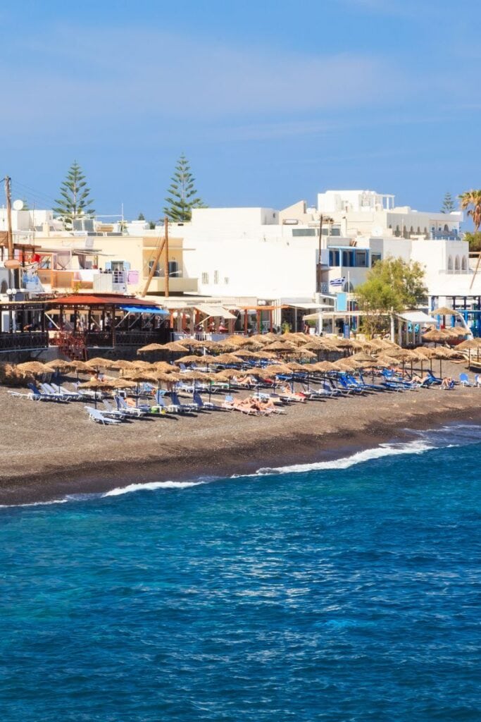 Beautiful Santorini beach with sunbeds, umbrellas, and scenic white architecture overlooking the Aegean Sea.