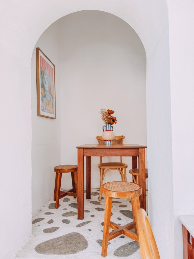 Small Greek-style dining nook with wooden table and stools, white walls, and decorative accents.
