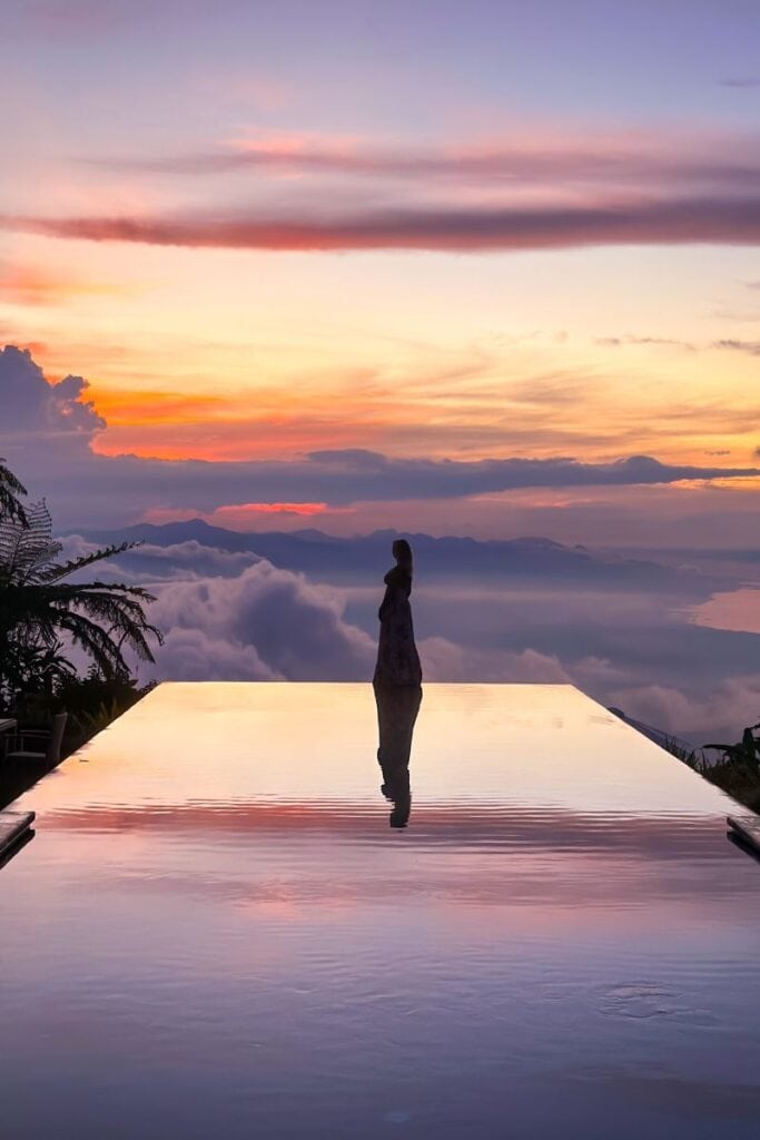 Woman enjoying sunset view over mountains from infinity pool in Munduk, Bali.