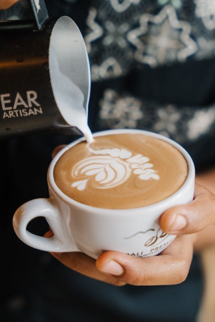 Barista pouring milk into a coffee mug with latte art design.