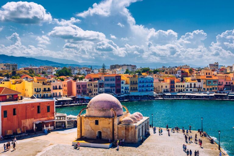 Colorful seaside town with historic buildings and a waterfront view under a partly cloudy sky.