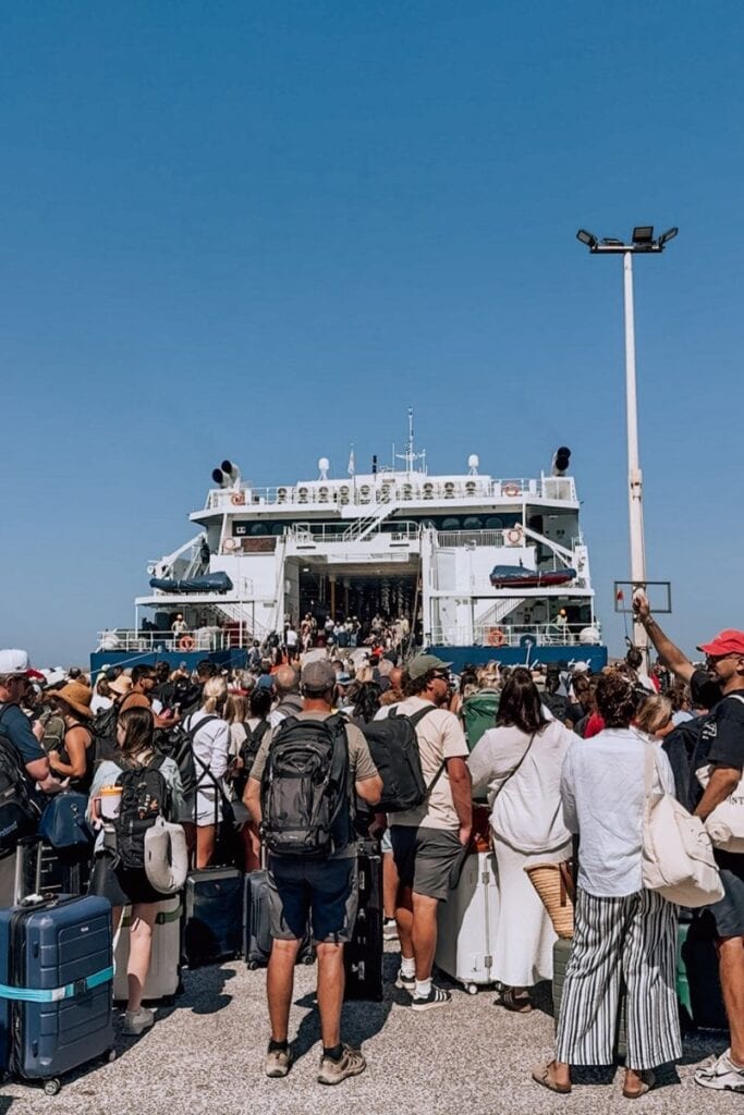 Crowded ferry terminal with travelers and luggage under clear blue sky.